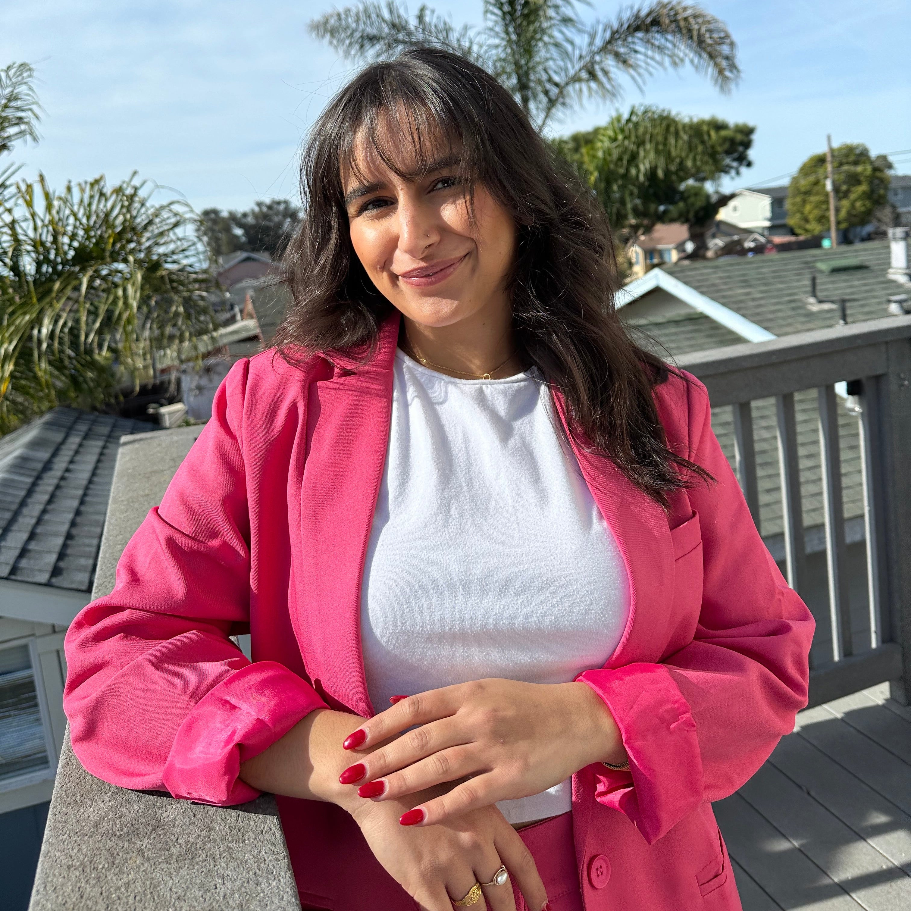 Woman in a pink jacket sitting outdoors with a clear blue sky and trees in the background
